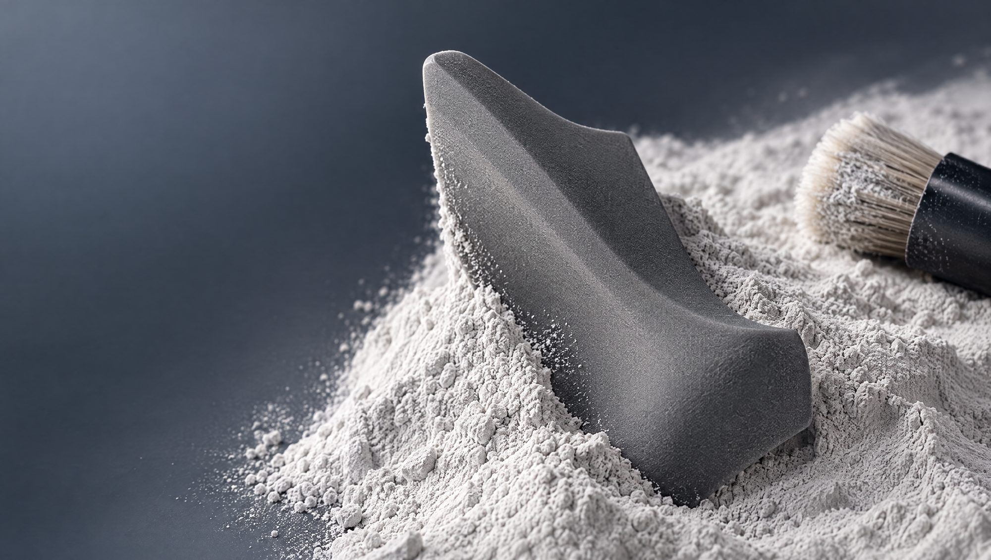 A grey nylon SLS part half buried in white powder, a brush clearing it