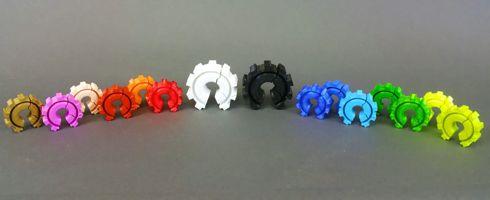 Row of 3D printed gear-shaped tokens in a dozen filament colors