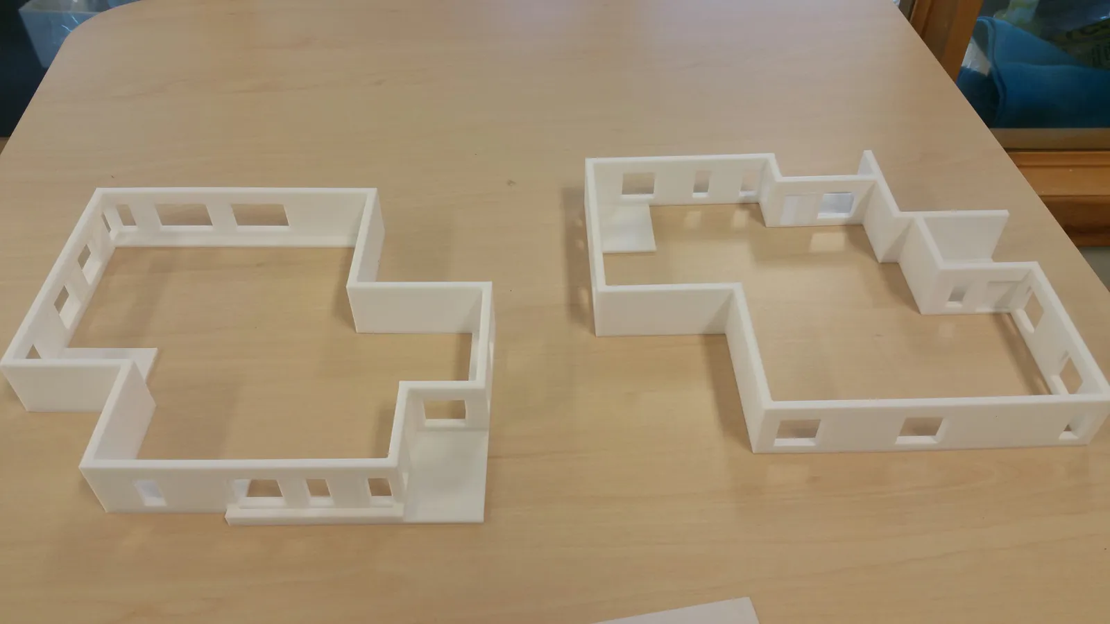Two white 3D-printed floor-plan models with walls, doorways and window openings on a wooden table.