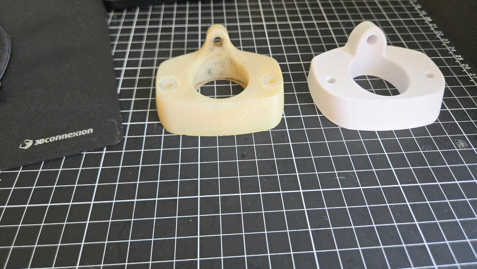 Pièce à bride jaunie et prototype imprimé blanc, avec des ouvertures centrales et des trous de fixation correspondants.