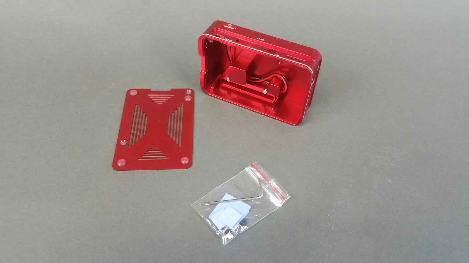 Photo originale du boîtier rouge en aluminium avec sa base retirée, les fixations intérieures et les accessoires d’assemblage.