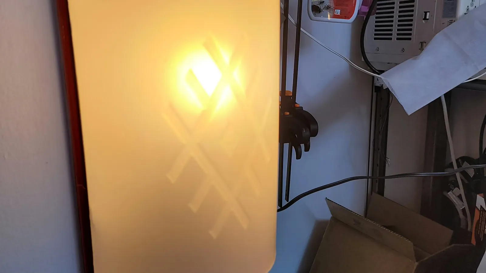 An assembled sconce lit, showing the etched pattern.