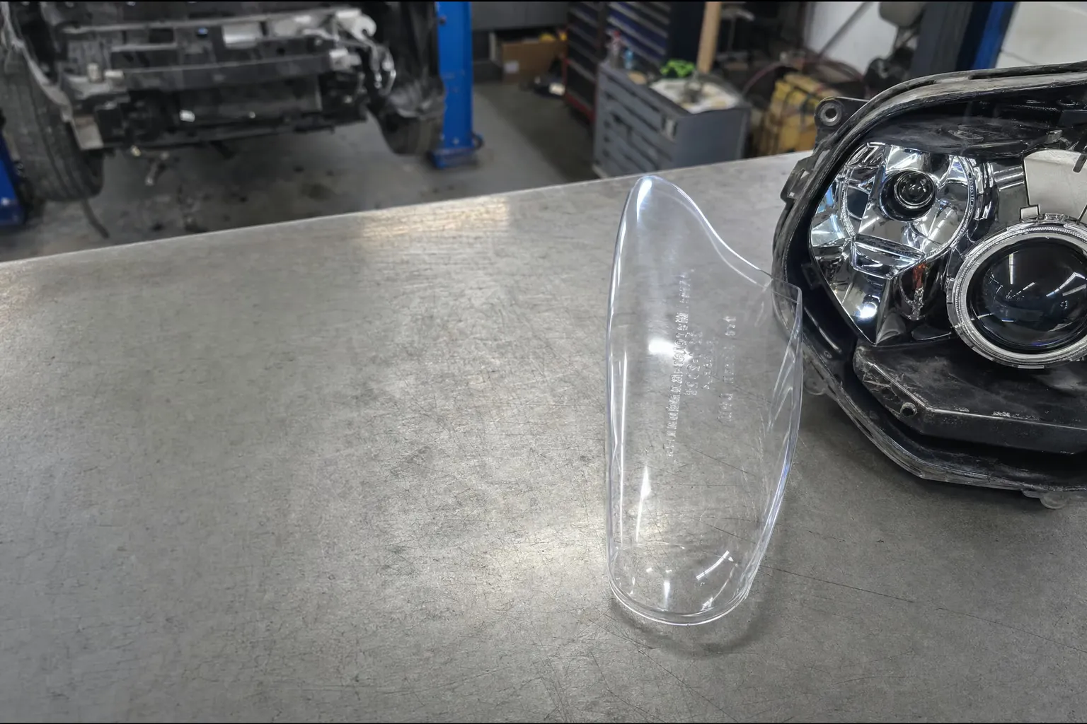 Couvercle de phare automobile en polycarbonate transparent sur un établi de garage, à côté d'un boîtier de phare