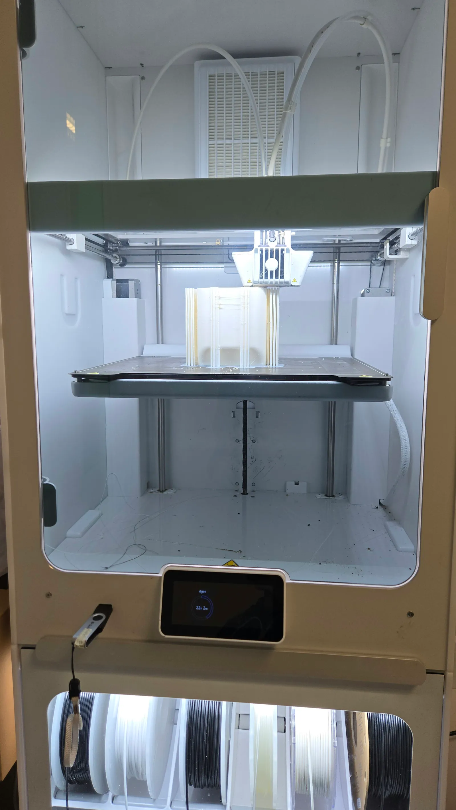 Enclosed FDM 3D printer mid-print with touchscreen and filament spool storage below
