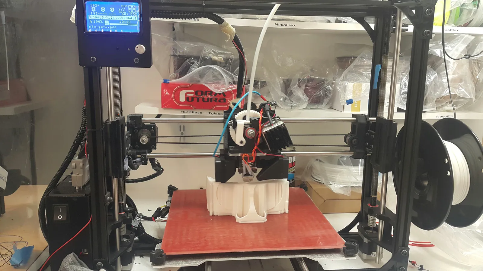 FDM 3D printer mid-print with dual extruder building a white PLA part on a red print bed