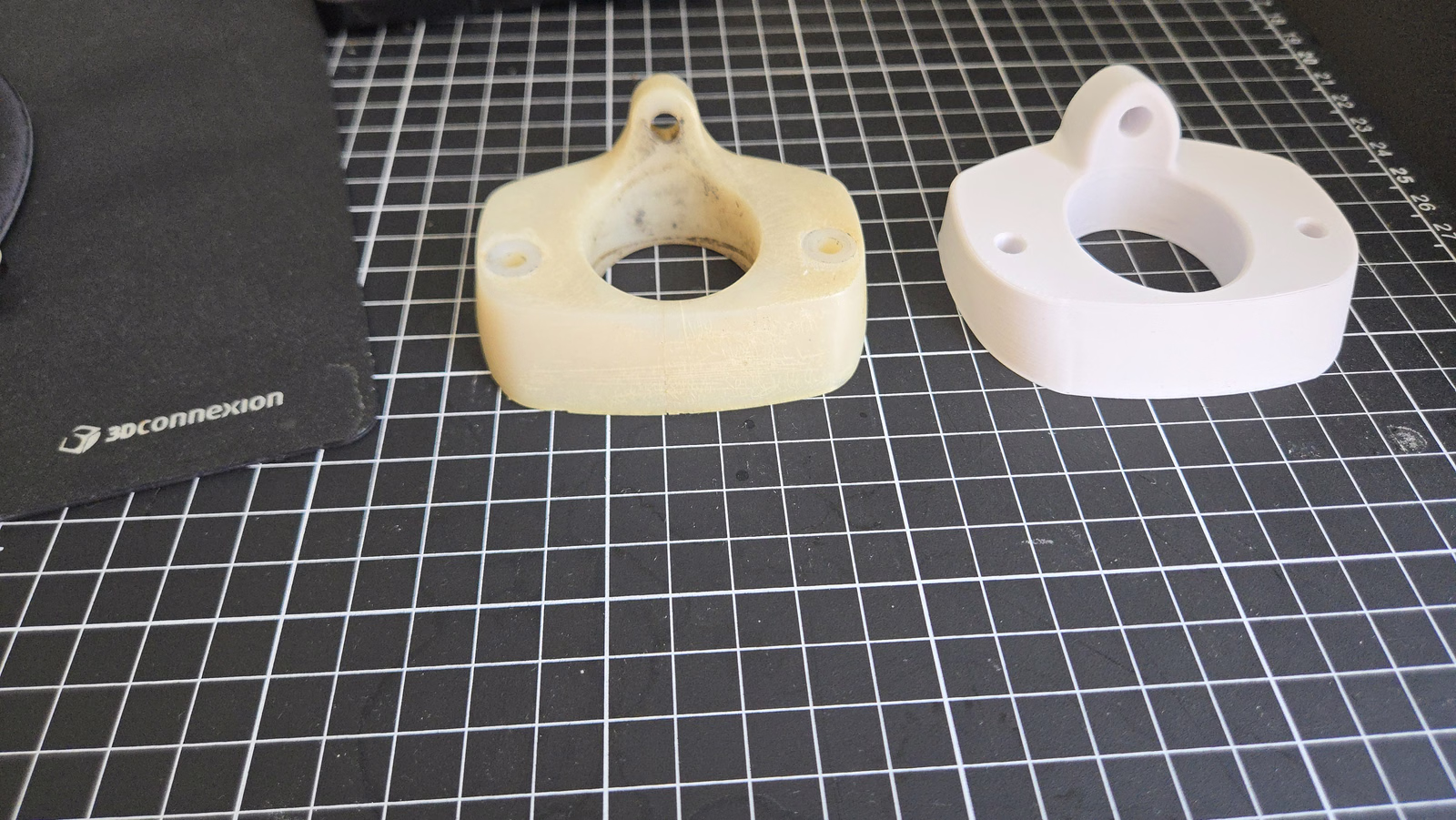 Yellowed flanged part and white printed prototype with matching centre openings and mounting holes.