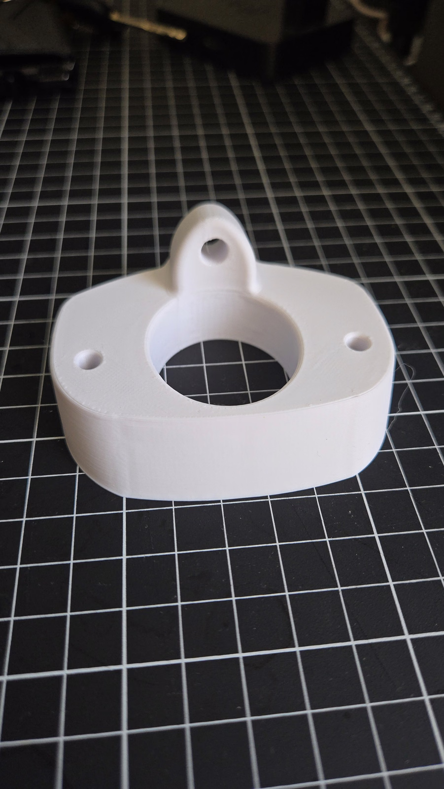 White 3D printed flanged bracket on a gridded work mat.